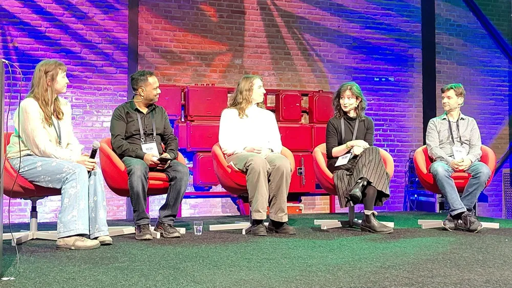 Madeleine on stage at ECIR 2026, sitting on a red chair with four other panelists